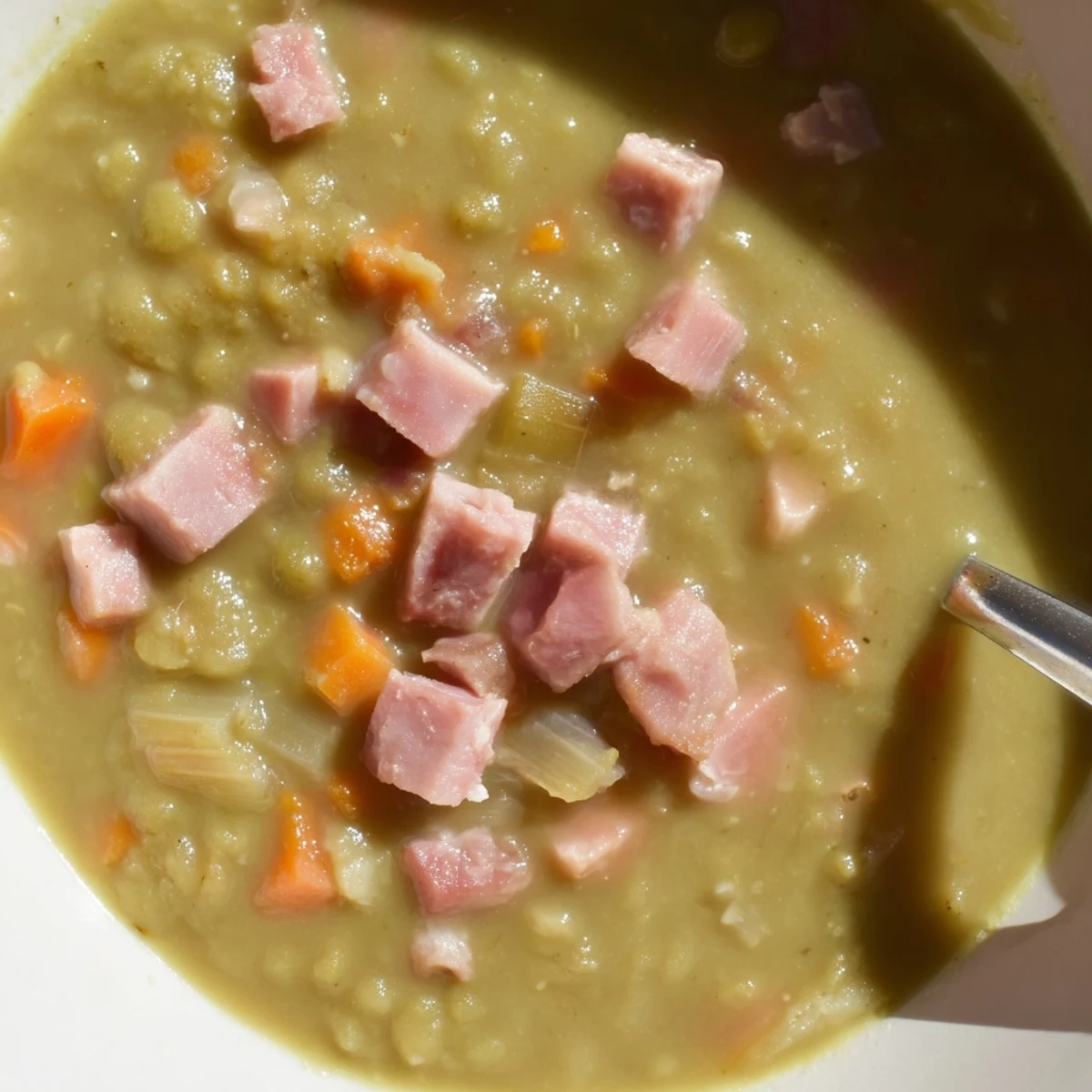 Creamy textured Hearty Split Pea and Ham Soup, seasoned perfectly and garnished with fresh herbs alongside bread.