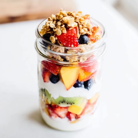 A close-up of a refreshing yogurt parfait featuring colorful fruit, granola, and creamy yogurt.