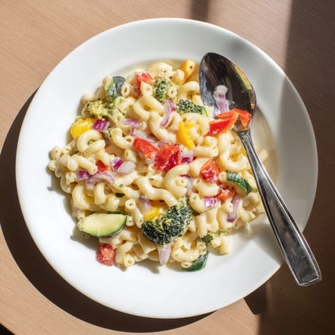 A close-up of Roasted Veggie Mac & Cheese reveals creamy cheddar sauce coating pasta and colorful roasted red peppers and broccoli florets.  