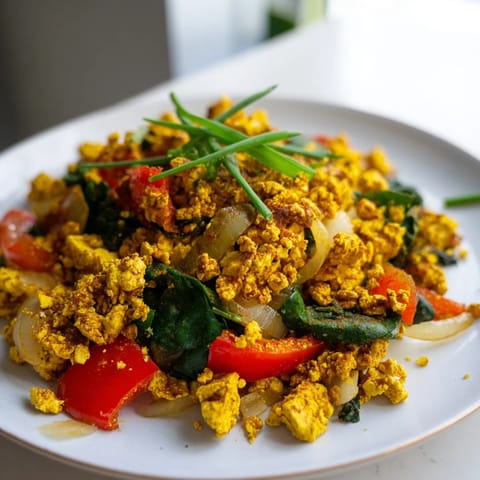 Close-up view of fluffy Tofu Scramble cooked with cumin and smoked paprika, served alongside a slice of whole-grain toast and avocado.